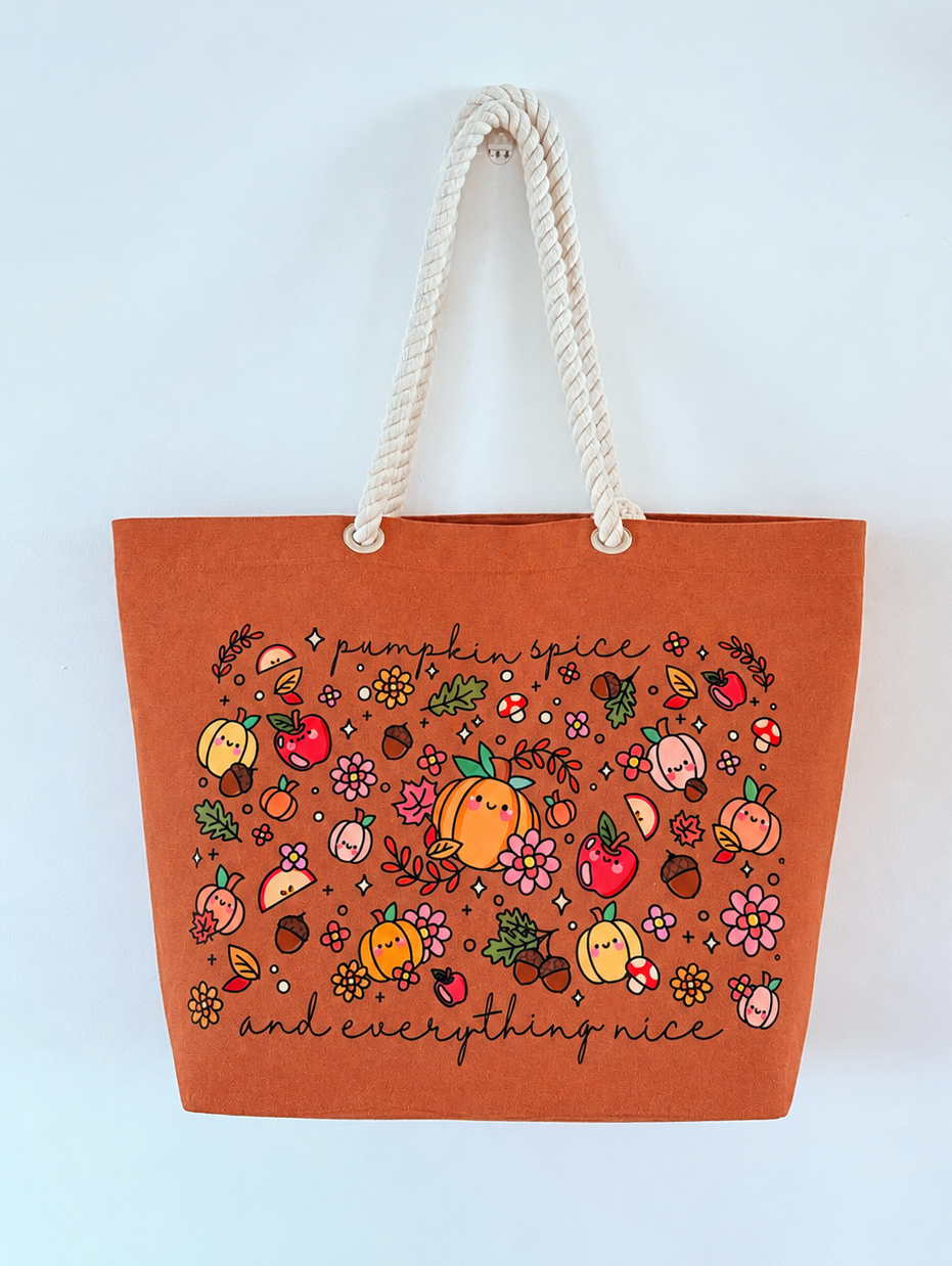 An orange canvas tote bag with cream rope handles, featuring a colorful autumn-themed illustration of pumpkins, apples, and leaves with the text 'pumpkin spice and everything nice' on a plain white background.