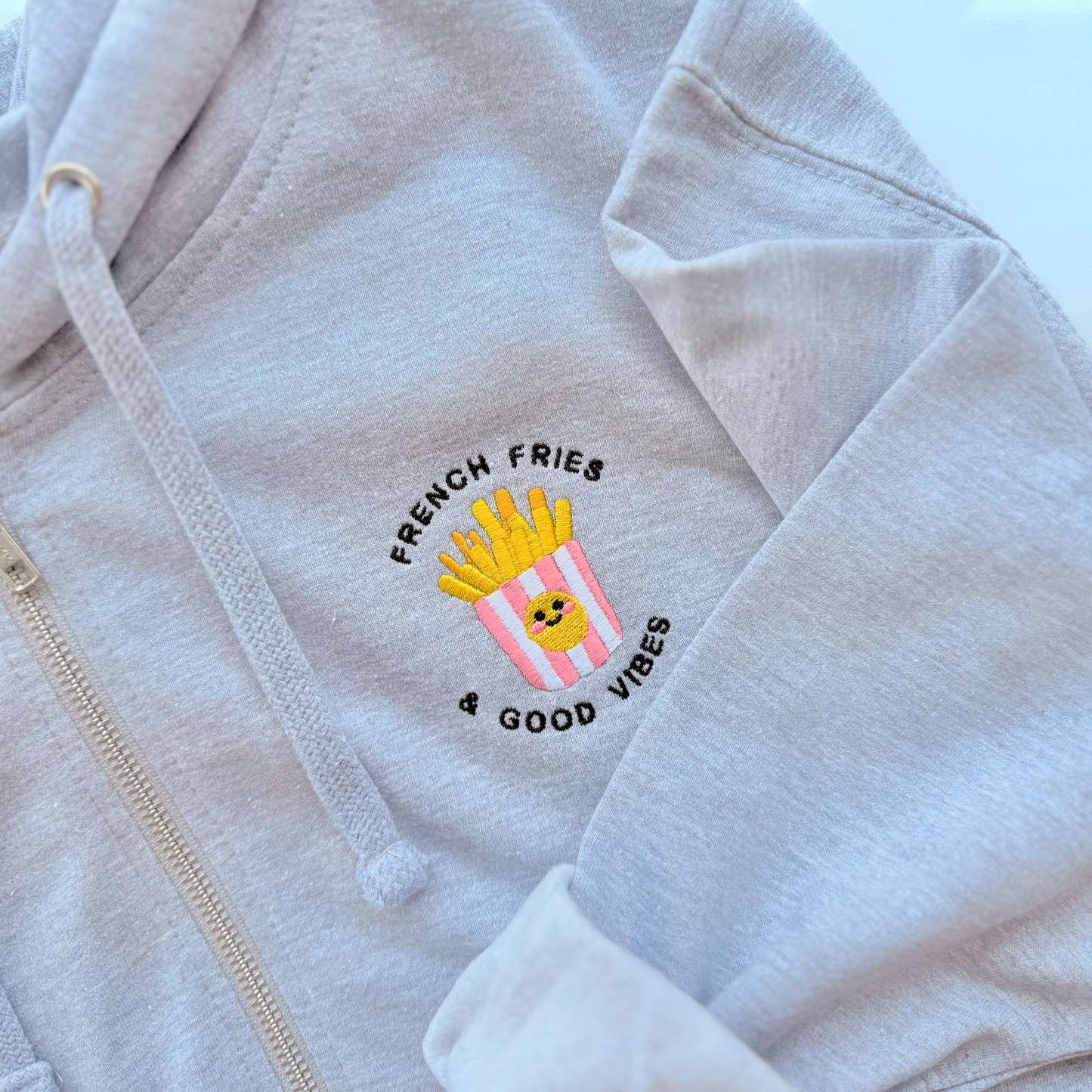 Light gray hoodie with a embroidered design on the chest featuring French fries and text.