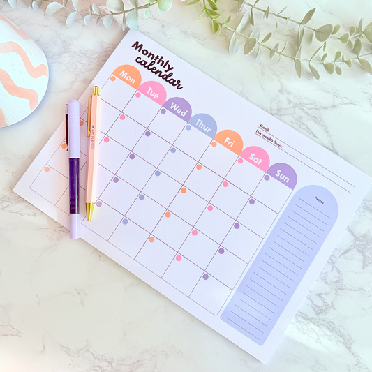 Monthly calendar with colorful days of the week on a marble surface with decorative items.