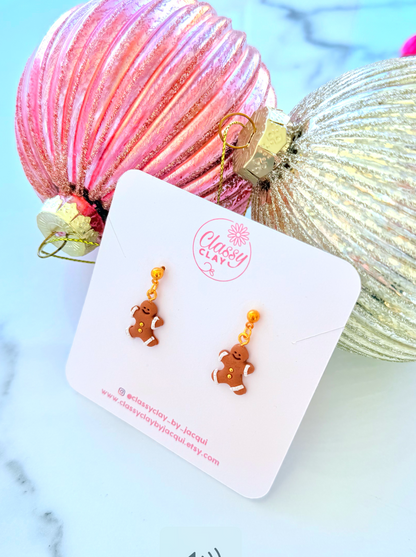 Gold gingerbread men earrings on a white card with 'Classy Clay' branding, set against a christmas themed decorative background.