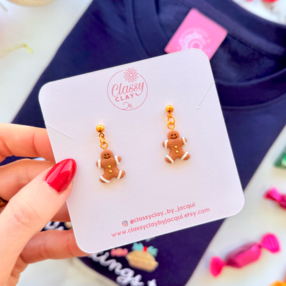 Gold gingerbread men earrings on a branded card held by a hand with red nail polish.
