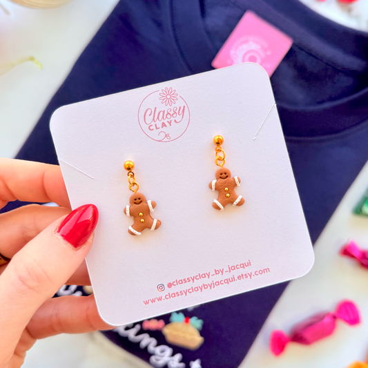 Gold gingerbread men earrings on a branded card held by a hand with red nail polish.