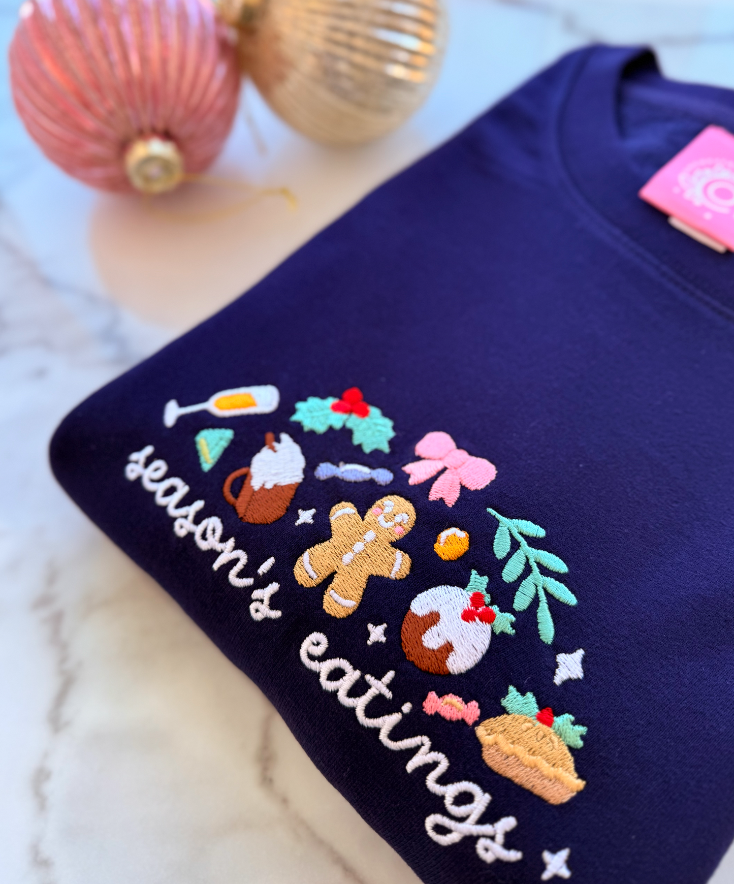 Navy blue shirt with festive design and 'season's eatings' text, surrounded by Christmas decorations.