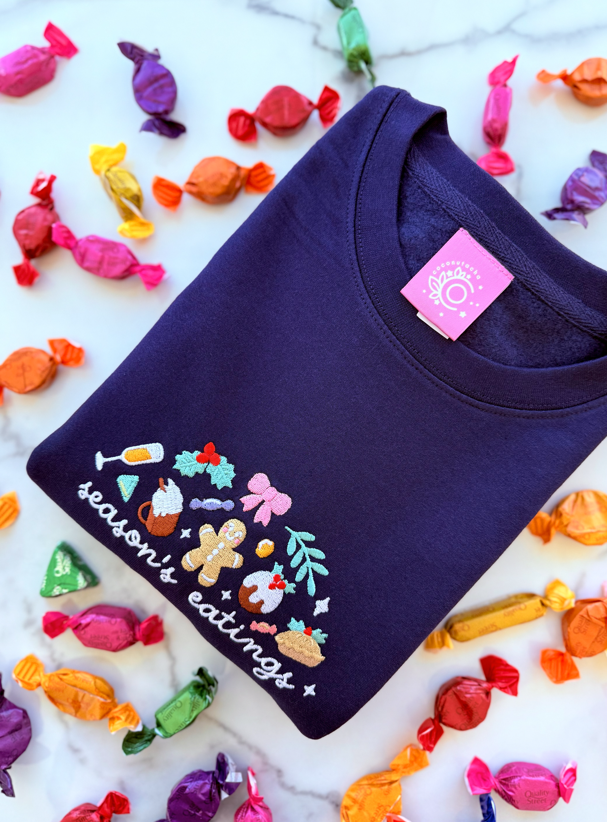 Navy blue sweatshirt with colorful graphics and text 'season's eatings' on a white background with candy decorations.