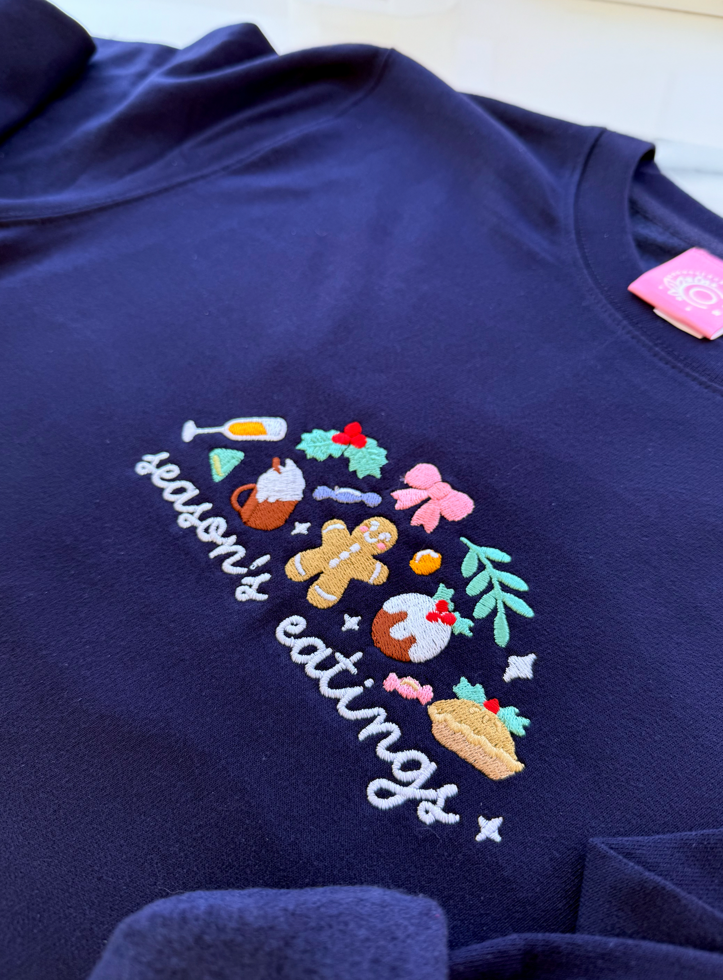 Navy blue sweatshirt with 'season's eatings' embroidered design on a white background