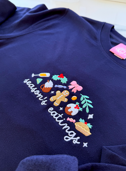 Navy blue sweatshirt with 'season's eatings' embroidered design on a white background