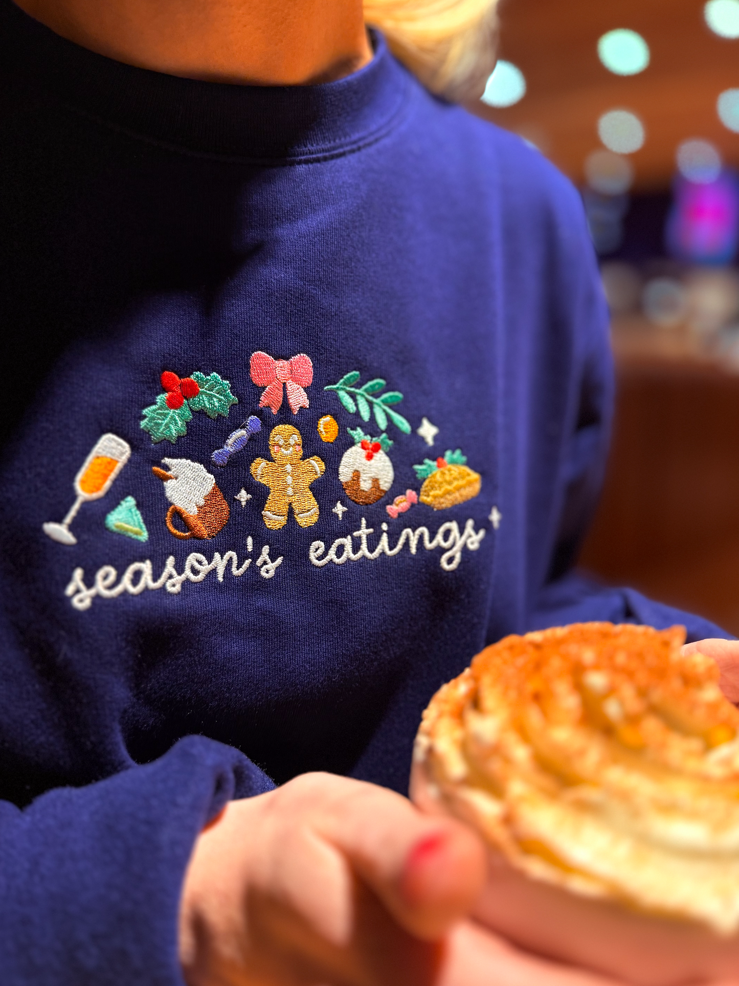 Person wearing a navy blue sweatshirt with festive design holding a pie.