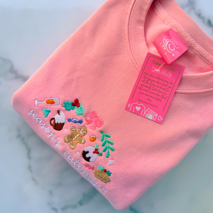 Pink sweatshirt with festive designs and a tag on a marble surface