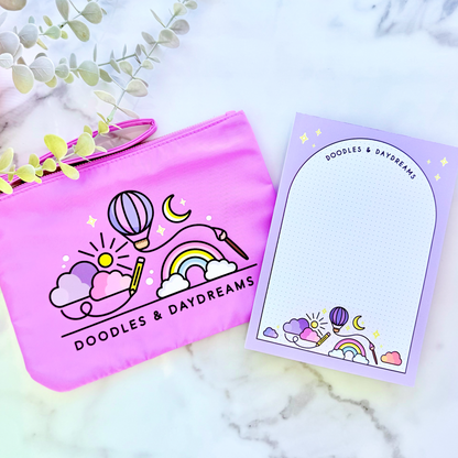 Pink pouch with 'Doodles & Daydreams' design on a marble surface with a card featuring similar design.