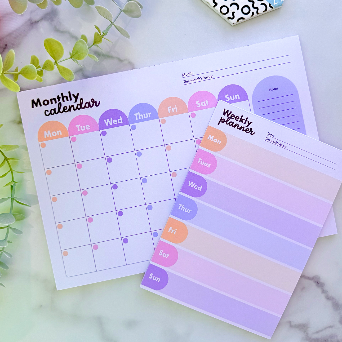 Monthly and weekly planner sheets with colorful design on a marble surface.