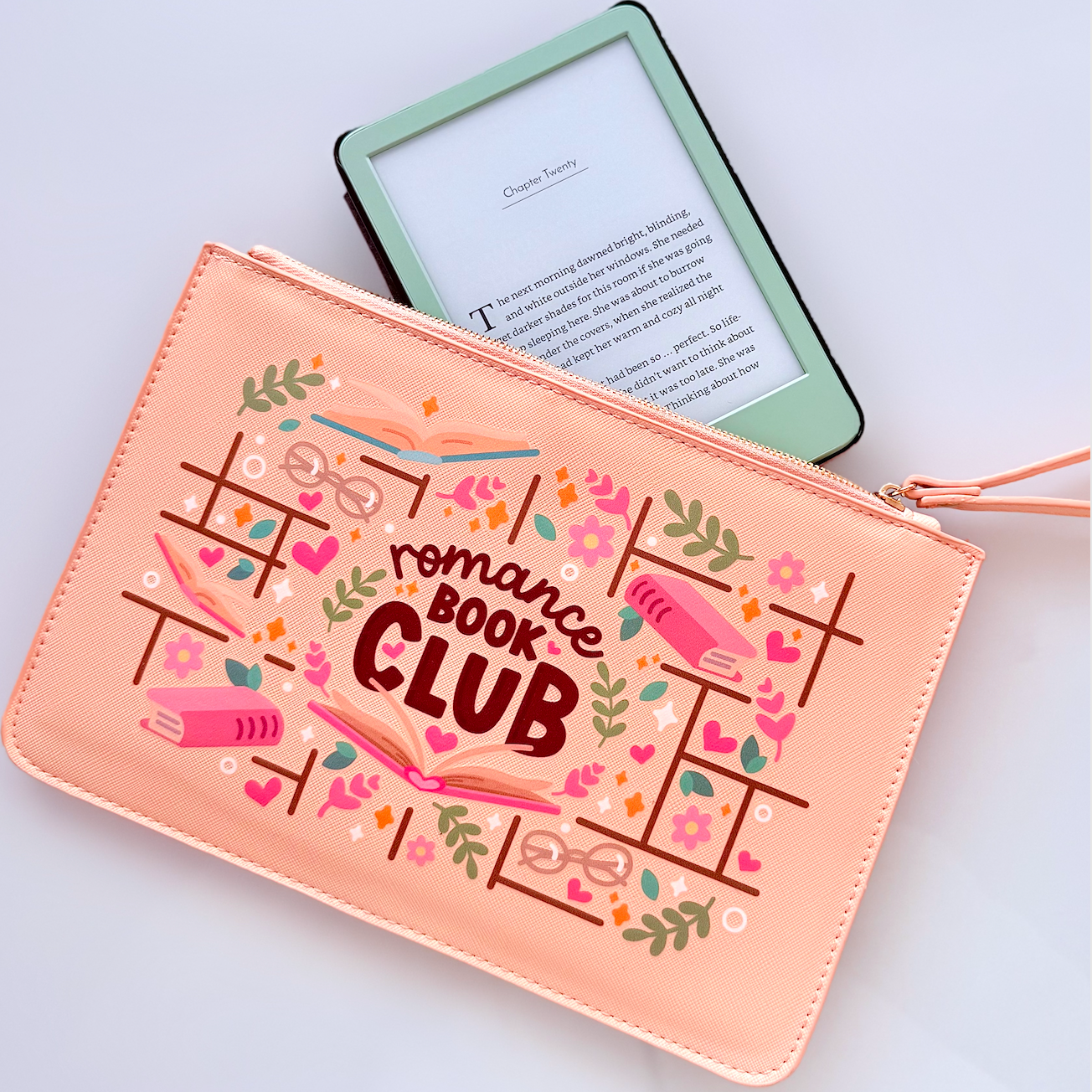 Pink pouch with 'romance book club' design next to a green e-reader on a light gray background
