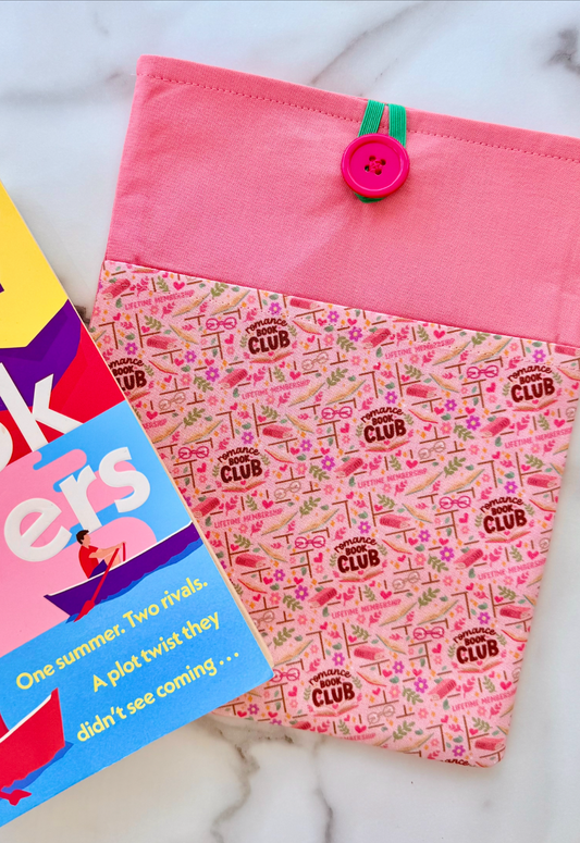 Pink fabric pouch book sleeve with 'Book Club' pattern next to a book on a white surface