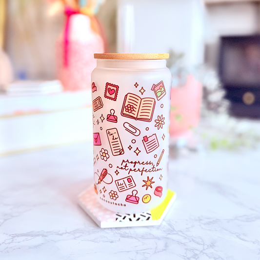 A frosted glass can cooler with a bamboo lid, decorated with pink and brown doodles and the text 'Happiness is perfection', sitting on a marble countertop in a brightly lit, blurred living room setting.
