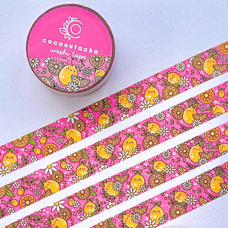 Two rolls of patterned washi tape displayed on an open notebook, with several strips laid out diagonally. The tape has a bright pink background with a retro pattern of yellow chicks, brown paisley, and small white flowers.