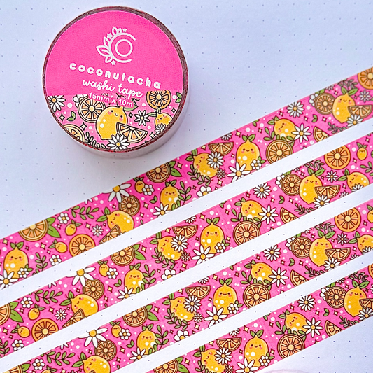 Two rolls of patterned washi tape displayed on an open notebook, with several strips laid out diagonally. The tape has a bright pink background with a retro pattern of yellow chicks, brown paisley, and small white flowers.
