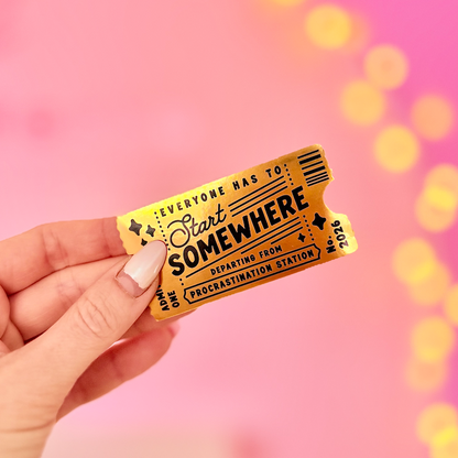 A hand holding a gold and yellow vintage-style travel ticket that reads 'Everyone Has to Start Somewhere' against a bright pink background with soft yellow bokeh lights.