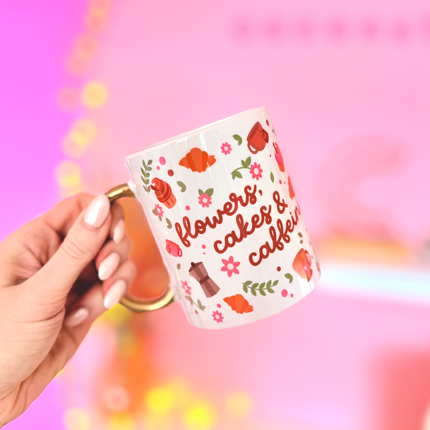Hand holding a mug with floral design and text against a pink background