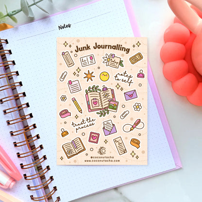 A rectangular planner sticker sheet titled 'Junk Journalling' with cute doodle illustrations and phrases like 'notes to self' and 'trust the process,' placed on an open lined notebook. The scene is styled with a coral phone, green leaves, and a pink pen.