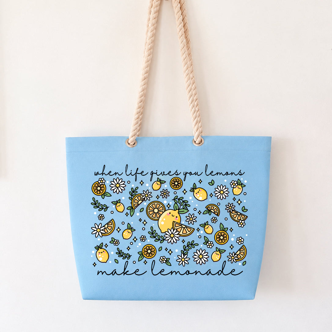 A light blue canvas tote bag with beige rope handles, featuring a yellow and green lemon-themed floral pattern with the text 'when life gives you lemon, make lemonade' on a plain white background.