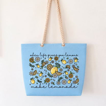 A light blue canvas tote bag with beige rope handles, featuring a yellow and green lemon-themed floral pattern with the text 'when life gives you lemon, make lemonade' on a plain white background.