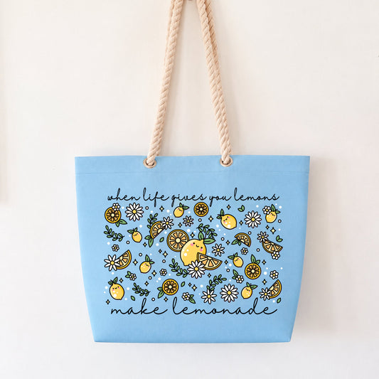 A light blue canvas tote bag with beige rope handles, featuring a yellow and green lemon-themed floral pattern with the text 'when life gives you lemon, make lemonade' on a plain white background.